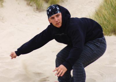 Young man in black sandboarding on beach dunes.